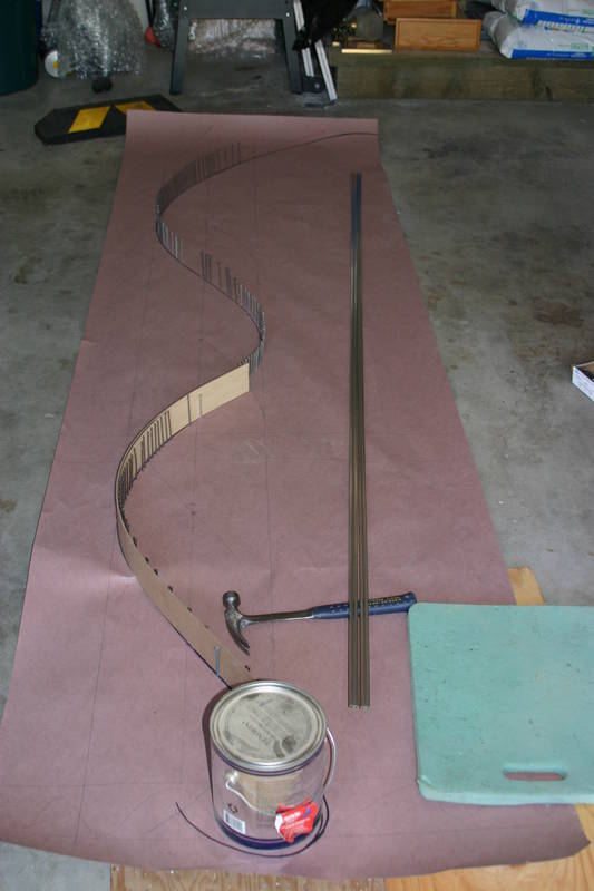 This was moved into the garage, where a variety of methods were used to bend the rail. Bending was more difficult than expected.  We used a paint can, nails into some plywood (a peg board), but mostly, one of my old bicycle wheels!