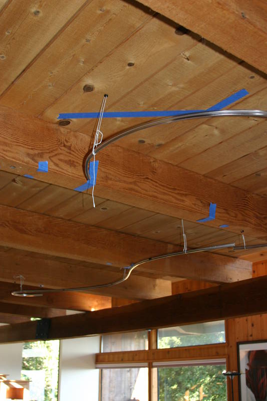 Basically bent, the two rails are hung from the ceiling with string to zero in on the location. The blue tape on the ceiling marks the location of the stairs in the loft, which is where the power will come from.